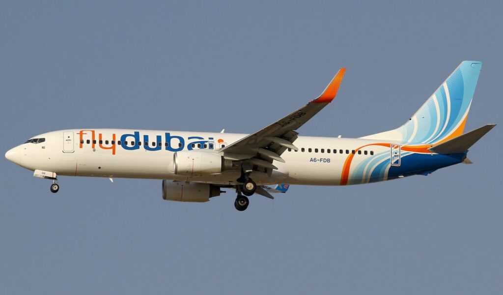Flydubai aircraft in flight against a clear blue sky, showcasing its colorful tail design and extended landing gear.